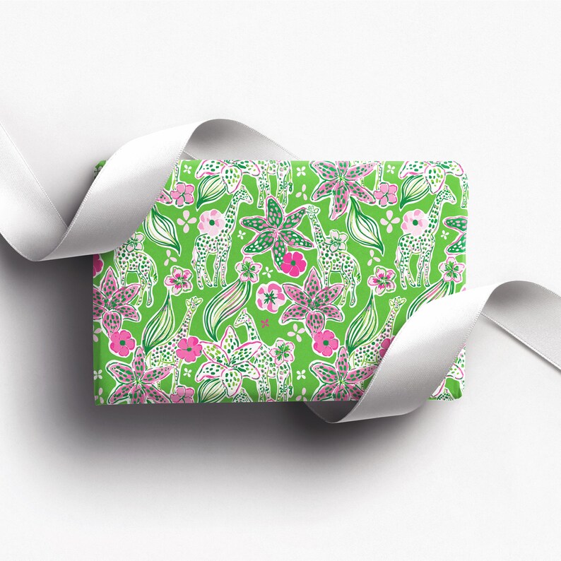 a gift wrapped in vibrant, tropical-themed wrapping paper featuring pink and white flowers and playful giraffes on a bright green background. A crisp white ribbon tied into a bow adds a classic, elegant touch to the lively and fun design.