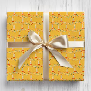 May include: A wrapped gift box with a yellow background featuring a repeating pattern of candles and string lights. The box is tied with a cream-colored ribbon and bow, creating a festive and decorative presentation.