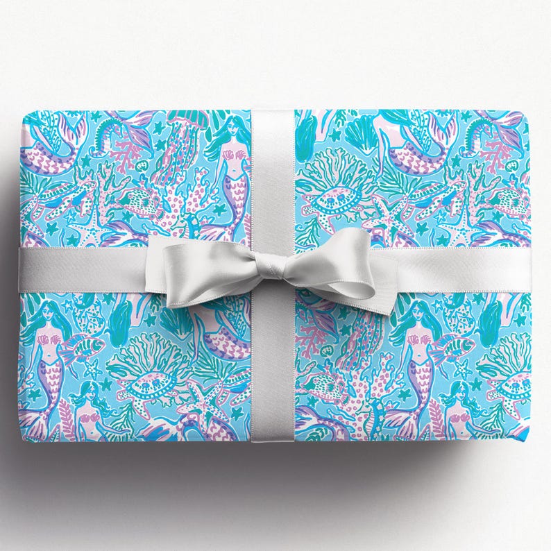 a gift wrapped in vibrant mermaid-themed wrapping paper featuring playful mermaids, sea creatures, and starfish in shades of blue, pink, and teal. A crisp white ribbon tied into a bow adds an elegant contrast to the whimsical gift wrap.