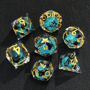 May include: Set of seven teal and gold dice with black cat illustrations. The dice are made of clear resin with a glittery finish.