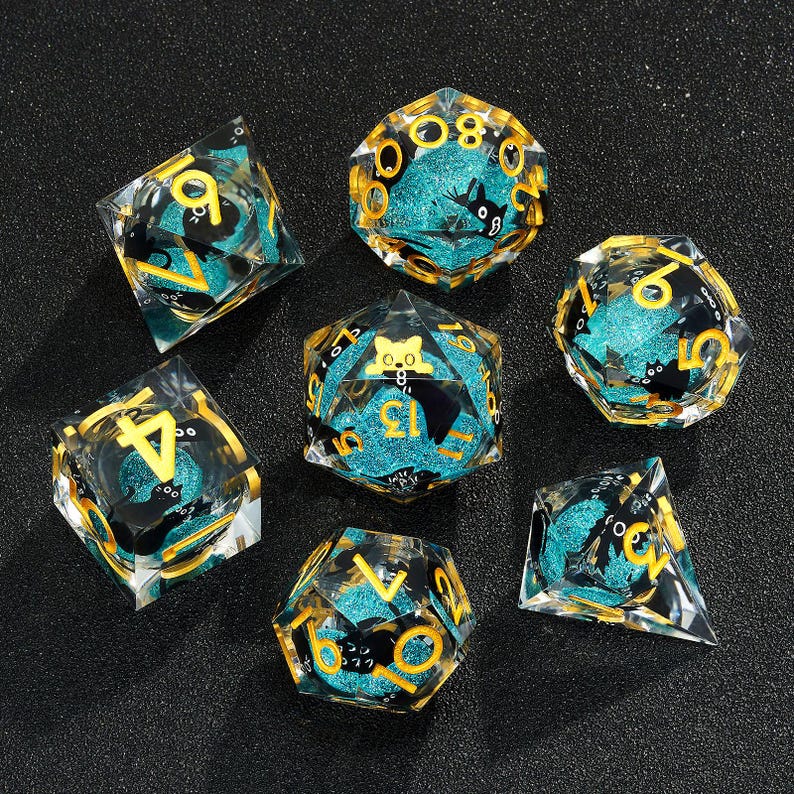 May include: Set of seven teal and gold dice with black cat illustrations. The dice are made of clear resin with a glittery finish.