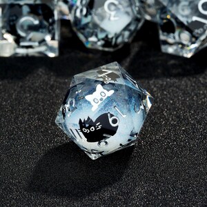 May include: A clear blue and white iridescent d20 dice with black cat faces on each side. The dice is made of resin and has a glittery finish.