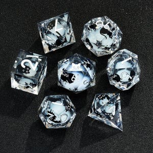 May include: Set of seven clear glass dice with black and white designs. Each die has a different design featuring a cat and numbers. The dice are on a black background.