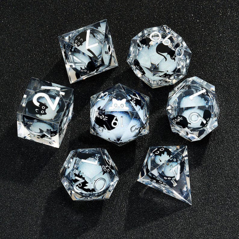May include: Set of seven clear glass dice with black and white designs. Each die has a different design featuring a cat and numbers. The dice are on a black background.