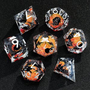 May include: Set of seven clear dice with black and orange glitter. The dice are numbered 1-6 and have a black cat design on each face.