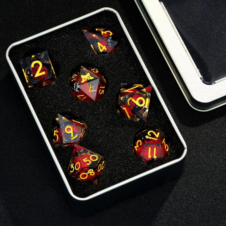 May include: A set of seven red and gold dice with black numbers in a black velvet lined metal box. The dice are translucent and have a swirl pattern.