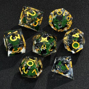 May include: Set of seven green and gold dice with black numbers and a black cat graphic on one die. The dice are made of clear acrylic with glitter embedded in the plastic.