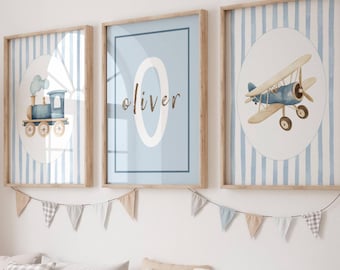 Puede incluir: Escena de habitación infantil con tres cuadros enmarcados que representan un tren, un avión y el nombre "Oliver". Las impresiones son azules y blancas. También se ve una gran jirafa tejida y un mueble de almacenamiento con contenedores.