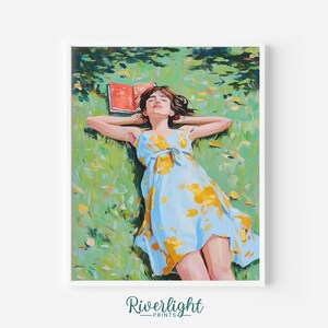 May include: A framed art print depicts a person lying in a grassy field, wearing a light blue dress with yellow floral accents. A book rests on the grass near the person's head. The artwork has a painterly style with a focus on color and light.