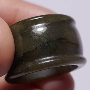 May include: A dark green ring with a wide band. The ring has a smooth, polished surface with natural variations in color and texture. The ring is a unisex accessory.