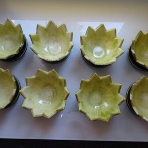 May include: Set of eight green and white ceramic bowls with a unique, starburst design. Each bowl has a scalloped edge and a smooth, glossy finish.