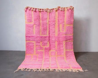 May include: A vibrant pink rug with a geometric design in a lighter peach color. The rug has a textured, plush appearance with a fringe along the bottom edge and tassels at the top. This decorative rug is suitable for home decor.