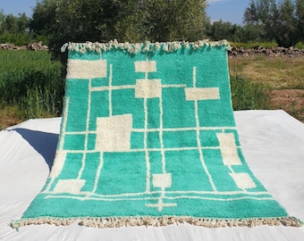 May include: A turquoise and white geometric patterned rug with a fringe border. The rug has a modern design with a grid pattern and white squares.