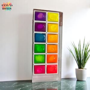 May include: A rectangular watercolour paint set with twelve vibrant colours, including purple, yellow, blue, green, and orange. The paint set is in a clear plastic case. The text "CANVAS DIGITS" is in the upper left corner.