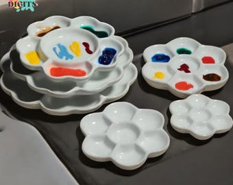 May include: White ceramic flower-shaped paint palettes. Some palettes contain colorful paint, including red, yellow, blue, and green. The text "CANVAS DIGITS" is visible in the upper left corner.