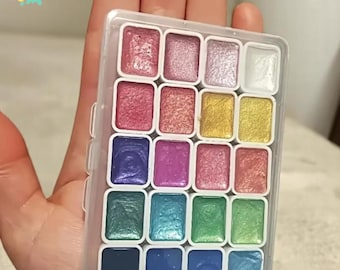 Puede incluir: Una paleta de pintura de acuarela de plástico transparente con 18 cubetas rectangulares llenas de varios colores metálicos. Los colores incluyen rosas, morados, azules, verdes y dorados. El texto "CANVAS DIGITS" está en la esquina superior izquierda.