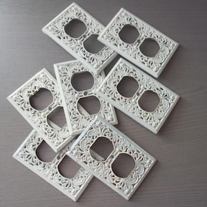 May include: Set of seven white decorative light switch covers with an ornate, floral design.