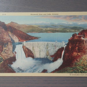 May include: Vintage postcard featuring Roosevelt Dam and Lake in Arizona. The image showcases a scenic view of the dam with water cascading down, surrounded by mountains and a lake under a colorful sky. The text "Roosevelt Dam and Lake, Arizona" is visible.