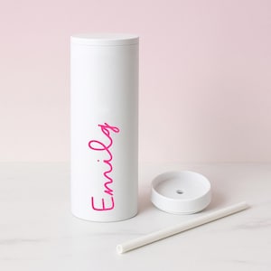 May include: White insulated tumbler with a lid, straw, and a separate lid piece. The tumbler has the name "Emily" in pink script. The tumbler is cylindrical and stands upright. The straw and lids are white.