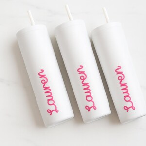 May include: Three white tumblers with pink text reading "Lauren". Each tumbler has a white straw and lid. The cylindrical tumblers are made of metal. Each tumbler is approximately 20 cm tall.