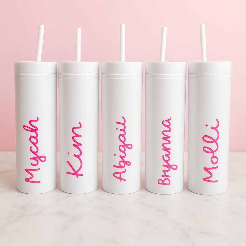 May include: Five white tumblers with pink names: Mycah, Kim, Abigail, Bryanna, and Molli. Each tumbler has a white straw. The background is a solid pink.