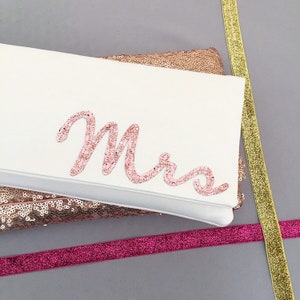 Ivory satin bridal clutch for wedding day.  The design on the front says MRS which is made from rose gold glitter.