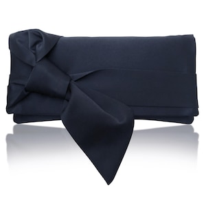 Op de afbeelding: Een marineblauwe satijnen clutch met een grote strik. De rechthoekige tas heeft een gevouwen ontwerp en een brede, decoratieve strik aan de voorkant. De strik is gemaakt van hetzelfde satijnen materiaal als de tas. De clutch is ontworpen om in de hand te worden gehouden.