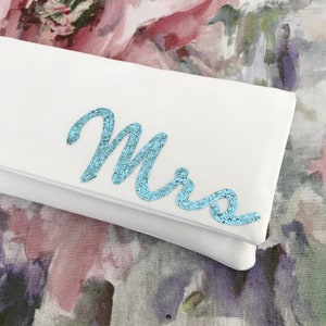 Ivory satin bridal clutch for wedding day.  The design on the front says MRS which is made from light blue glitter.