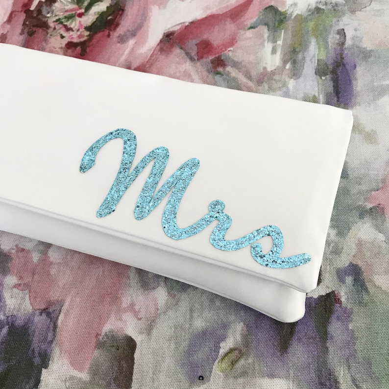 Ivory satin bridal clutch for wedding day.  The design on the front says MRS which is made from light blue glitter.