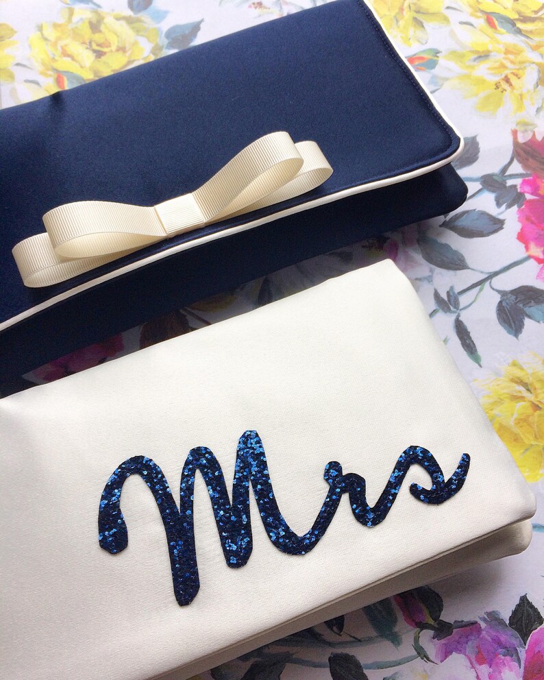 Ivory satin bridal clutch for wedding day.  The design on the front says MRS which is made from navy glitter.