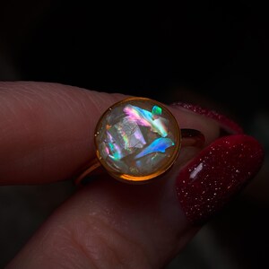 May include: A gold ring with a round iridescent opal-like stone set in a bezel setting.