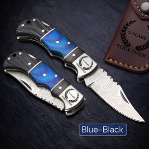 May include: Two folding knives with blue and black handles and silver blades. The handles have a blue wood grain design and are accented with silver and white details. The blades have a unique pattern. The text "5 YEARS TOGETHER" is on the blade. The text "Blue-Black" is at the bottom.