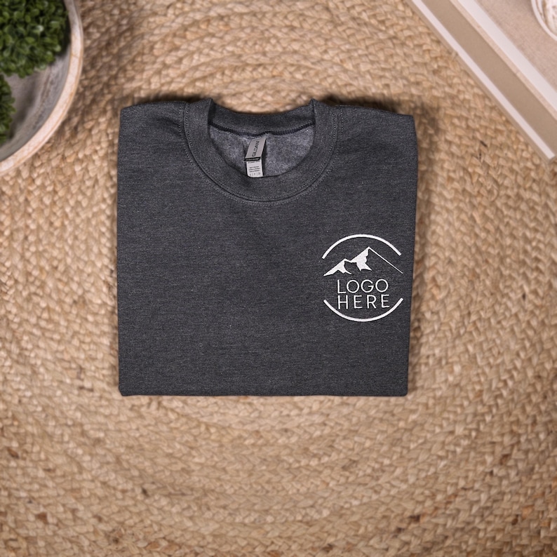 May include: A dark gray sweatshirt with a white circle logo featuring a mountain range and the text "LOGO HERE".