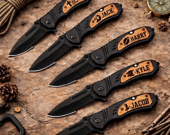 May include: An overhead shot of five black folding knives with wooden handles. Each handle is engraved with a name and a small graphic. The knives are arranged on a textured, brown surface, with a compass and rope in the background.
