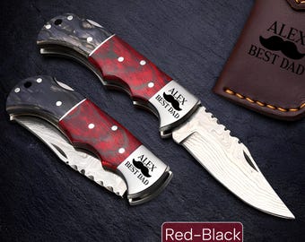 May include: Two folding knives with red and black handles and silver blades are displayed. The knives have the text "ALEX BEST DAD" engraved on the blade. A brown leather case with the same text is also visible. The image has the text "Red-Black".