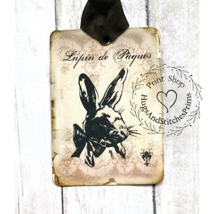 May include: A vintage-style tag with a black and white illustration of a rabbit wearing a bow tie. The tag has the text "Lapin de Paques" and a stamp that says "Hugs And Stitches Prints Shop".