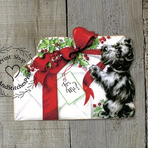 May include: A die-cut paper ornament featuring a white envelope tied with a large red ribbon and green holly berries. A small light green gift tag with the handwritten text For me? hangs from the ribbon, next to a black and white terrier dog.