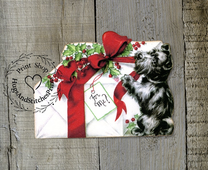 May include: A die-cut paper ornament featuring a white envelope tied with a large red ribbon and green holly berries. A small light green gift tag with the handwritten text For me? hangs from the ribbon, next to a black and white terrier dog.