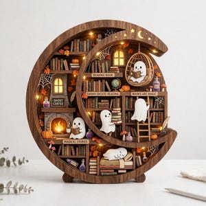 May include: A crescent moon-shaped wooden bookshelf diorama featuring illuminated miniature rooms with ghosts, books, a fireplace, and hanging chairs. Text labels include READING NOOK, SHHHH GHOSTS READING, BOOKS ARE MAGIC, GHOST COFFEE, and MAGICAL STORIES.