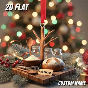 May include: A Christmas ornament with a wooden tree design, a red ribbon, and a wooden base. The base holds a loaf of bread, a bowl of flour, jars, and a whisk. The name "Anna" is on a tag. The text "2D FLAT" and "CUSTOM NAME" are also visible.