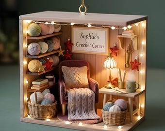 May include: A miniature crochet corner scene in a wooden box, featuring a small armchair, yarn, and a sign that reads "Sophia's Crochet Corner." The scene is illuminated by fairy lights and includes a small table with a lamp and a mug.