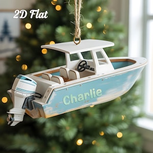 May include: A wooden boat ornament with a white cabin, blue hull, and a black steering wheel. The boat has the name "Charlie" in light blue lettering on the side. The ornament is suspended by a natural twine string.