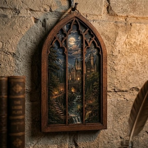 May include: A wooden framed wall art piece depicting a nighttime landscape with a castle, mountains, and a full moon. The artwork is framed in a dark brown, arched window shape and hangs on a textured stone wall.