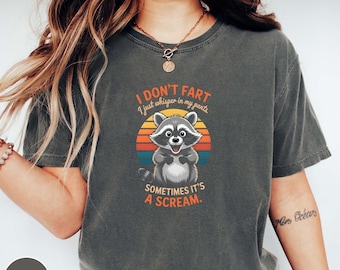 Könnte beinhalten: Dunkelgraues T-Shirt mit einem Waschbär-Cartoon und dem Text "I DON'T FART I just whisper in my pants SOMETIMES IT'S A SCREAM." Das Design beinhaltet einen Sonnenuntergang.