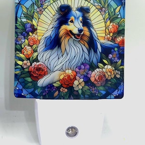 May include: A stained glass night light featuring a blue and white Sheltie dog surrounded by colorful flowers. The night light is white and has a small light bulb in the center.