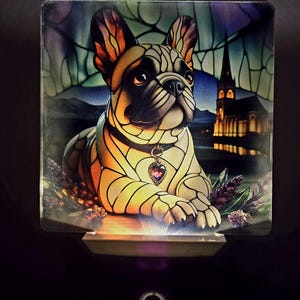 May include: A stained glass nightlight featuring a French bulldog with a purple heart pendant. The dog is sitting in a field of lavender with a church in the background.