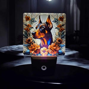 May include: A stained glass nightlight featuring a Doberman Pinscher dog with a floral design. The nightlight is illuminated and casts a warm glow.