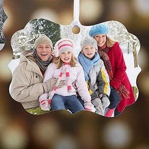 May include: A family portrait ornament featuring a smiling family of four in winter attire. The ornament has a scalloped edge and a hole for hanging. The family is wearing winter coats, hats, scarves, and gloves, set against a snowy background.