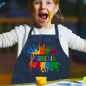 May include: A navy blue child's art smock with a colorful paint splatter design and the name "Amelia" printed in a rainbow font.