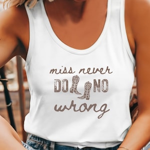 May include: White tank top with the text "miss never do no wrong" in brown lettering. The design includes two brown cowboy boots. The top is a casual, sleeveless style.